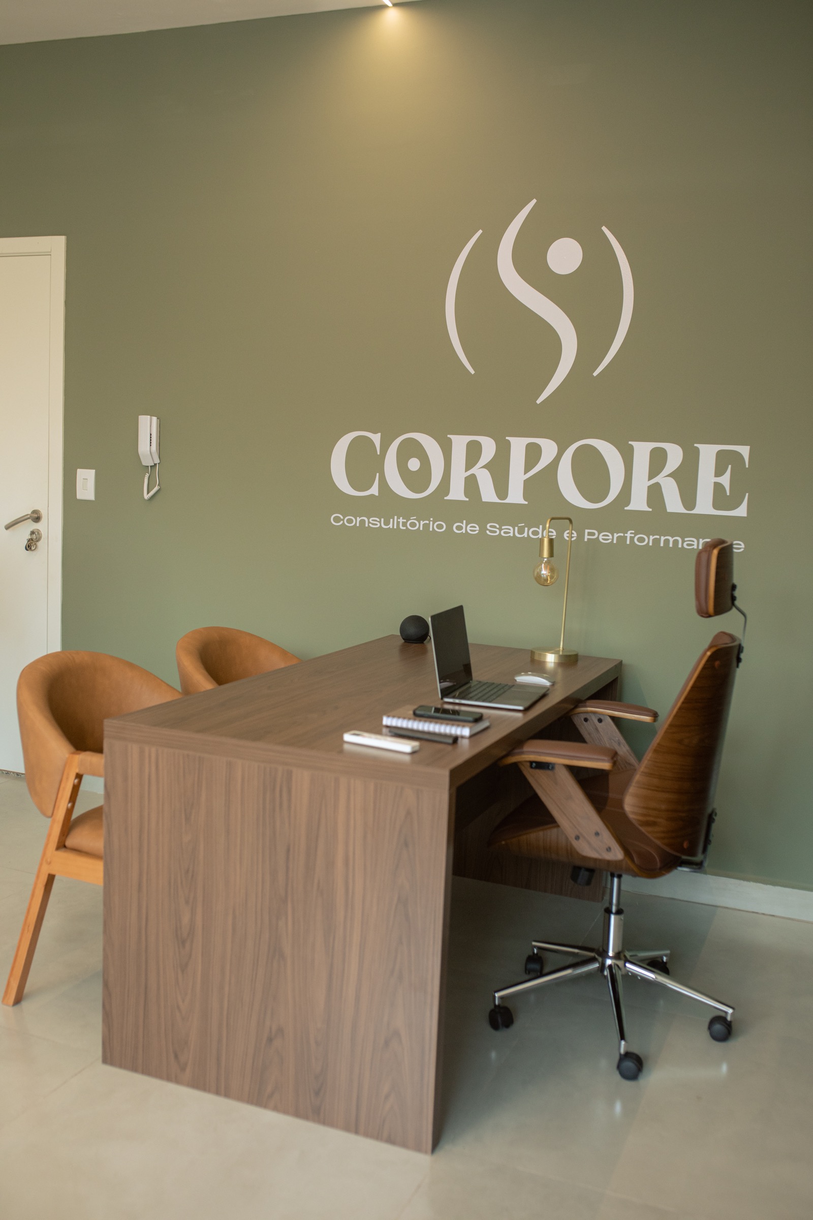 Consultório CORPORE com mesa, cadeiras e marca na parede